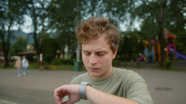 Young blond colored-eyed boy looks at his wristwatch and conveys that the time is too late, looks at the camera and shakes his head