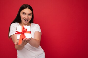 Shot of attractive positive smiling young brunette woman isolated over colourful background wall wearing everyday trendy outfit holding gift box and looking at camera