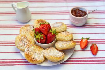 Syrniki or cottage cheese fritters with strawberry jam on a white plate.	