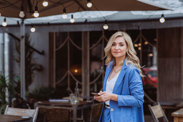 Beautiful woman businesswoman in a blue suit with a smartphone in her hands, teleworking. Soft selective focus.