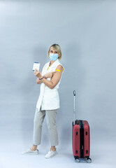 Tourist women ready for safe summer vacation. Studio portrait holding suitcase Wearing a mask raising arm vaccination record card after getting vaccinated with COVID-19 Coronavirus vaccination concept