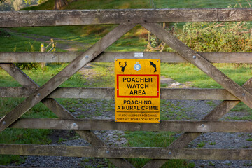 Poacher Watch Area sign in the British countryside.The sign is on a wooden gate.