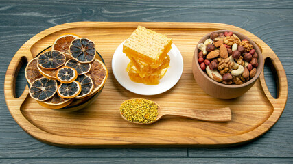 assortment of nuts and assorted dried citrus fruits and fresh floral honeycomb honey on kitchen wooden board. useful vitamin food for the human body