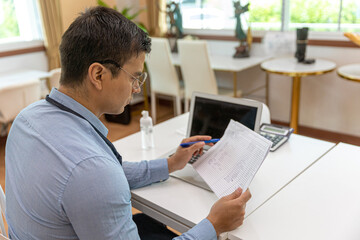 Young male owner is using computer notebook to check his stocks and goods in his startup bakery or caf&eacute; shop at the end of the day. Young entrepreneur working on his account and coming orders