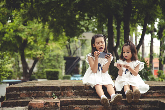 Concept kids and gadgets. Two little girls siblings sisters look at the phone. They hold a smartphone watch videos, learn, play games, speak online. Internet for children.