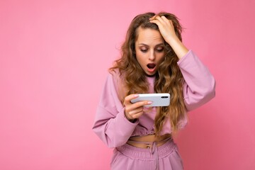 Photo of attractive crazy amazed surprised young woman wearing casual stylish clothes standing isolated over background with copy space holding and using mobile phone looking at camera - obrazy, fototapety, plakaty