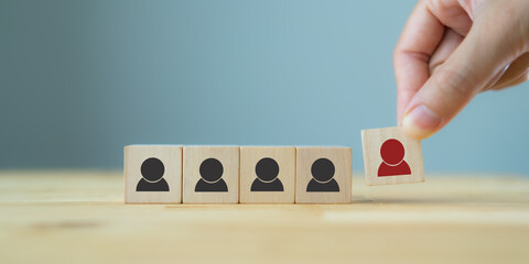Human resource management, recruitment and target customer business concept. Man's hand puts wooden cube red person which standing on crowd with black person symbol. Blue background and copy space.