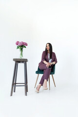 a business woman psychologist in a red suit is sitting in a chair on a white background next to a table with flowers