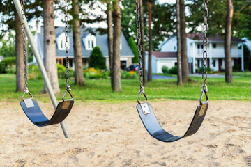 Playground with swings for children in the public park with houses in background.