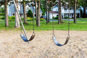 Playground with swings for children in the public park with houses in background.