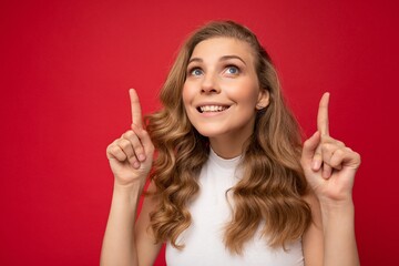 Photo of young positive happy smiling beautiful woman with sincere emotions wearing stylish clothes isolated over background with copy space and pointing at free space for advertising
