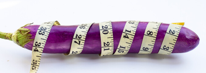 Long purple eggplant wrapped in measuring tape on white background. - obrazy, fototapety, plakaty