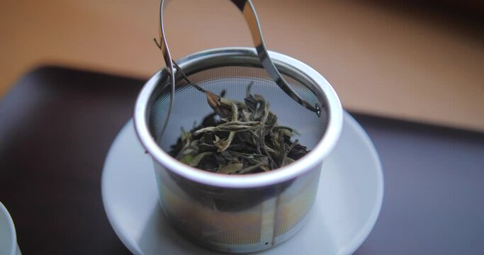 Dried Bai Mudan Tea Leaves In A Metal Teapot Filter Place On White Saucer. - close up
