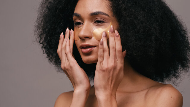 african american woman applying collagen eye patches isolated on grey