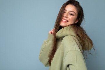 Portrait of young beautiful smiling girl in stylish hipster green hoodie. Sexy carefree woman posing near blue wall. Positive model having fun