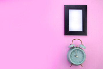 Top view of an alarm clock and blank photo frame in isolated pink background.