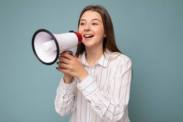 Portrait of beautiful nice positive happy smiling dark blonde young woman with sincere emotions wearing casual white striped shirt isolated over blue background with free space and shouting into