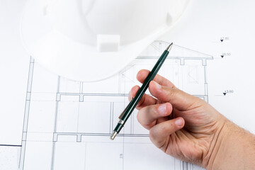 Spinning a pen on the architectural plan with a white safety helmet. Thinking about design. Architectural background photo. Drawing an architectural plan.