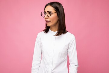 Attractive sad upset sorrowful young brunet woman wearing everyday stylish clothes and modern optical glasses isolated on colorful background wall looking to the side