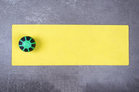 Flat Lay Of Yellow Yoga Mat With Medical Ball On Concrete Floor. Med Ball On Fitness Mat Spread Out On Cement Floor