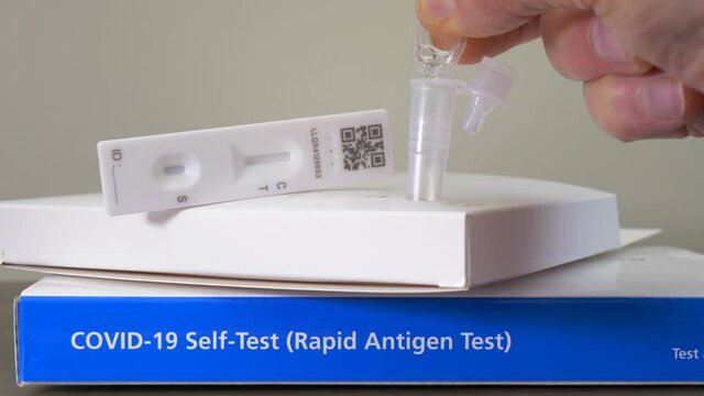 Closeup POV shot of a man&rsquo;s fingers starting to use a Covid-19 self-test (rapid antigen), by squeezing drops of liquid into a tube with a sealing cap.