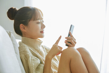 自宅でスマートフォンを操作する若い女性