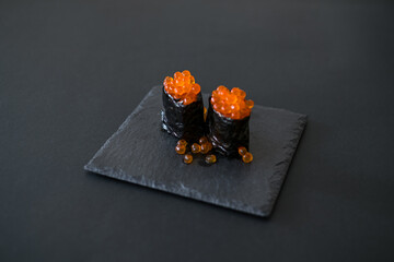 Gunkan Maki with salmon caviar in restaurant served on black board. Isolated on black background. Japanese traditional food. High quality photo
