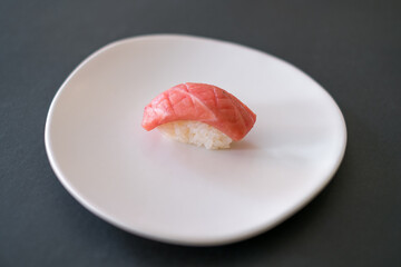 Sushi Nigiri with raw tuna served on white plate. One sushi piece on the black background. Japanese traditional food. 