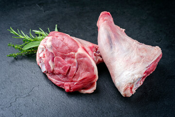 Raw traditional lamb shank with herbs offered as close-up on a black board with copy space