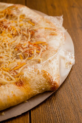 Simple cheese pizza on a cardboard base on a wooden table surface. Frozen product. Italian style fast food.