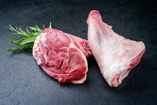 Raw traditional lamb shank with herbs offered as close-up on a black board with copy space