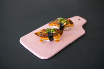 Japanese Sushi - Two Unagi Nigiri Sushi on light-pink board. Sushi pieces served on ight-pin slate isolated on black background. Sushi with backed eel