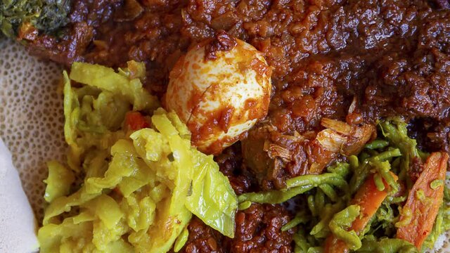 Pan across Injera served with chicken, egg, doro wat, berbere, vegetables and lentils. Injera, a traditional staple food of Ethiopia, is a sourdough flatbread made from teff flour.