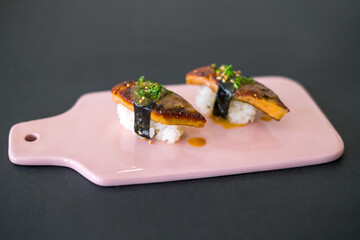 Japanese Sushi - Two Unagi Nigiri Sushi on light-pink board. Sushi pieces served on ight-pin slate isolated on black background. Sushi with backed eel
