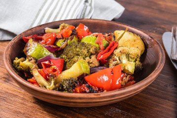 Ready-baked vegetables. Baked broccoli, peppers, onions and tomatoes in a plate on the table, close-up