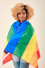Young afro woman looking into the camera while covering with a gay pride flag.