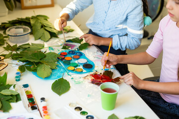 Girls paint patterns autumn leaf. Gouache, brush and various autumn leaves on a wooden table. Children's art project. Colorful Hand-painted on dry autumn leaves