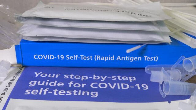 Closeup POV reverse dolly shot of an unbranded Covid-19 rapid antigen, self-test kit, with contents and user guide laid out on a table.