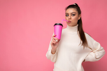 Photo of attractive surprised young happy brunette woman wearing everyday stylish clothes isolated over colourful background wall holding paper cup for cutout drinking tea looking at camera