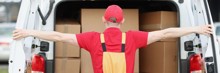 Male courier in uniform opening minivan with many cardboard boxes