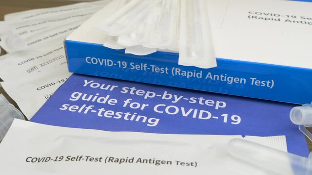 Closeup POV circular dolly shot of an unbranded Covid-19 rapid antigen, self-test kit, with contents and user guide laid out on a table.