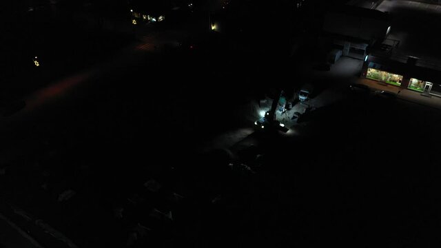 Aerial view of excavator demolishing a building, in middle of a dark city - circling, drone shot