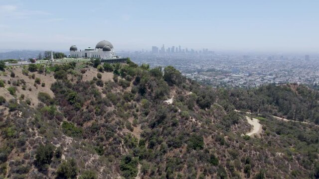Aerial dolly-in shot of Griffith Observatory in foreground and Los Angeles skyline in background. Griffith Park, CA.