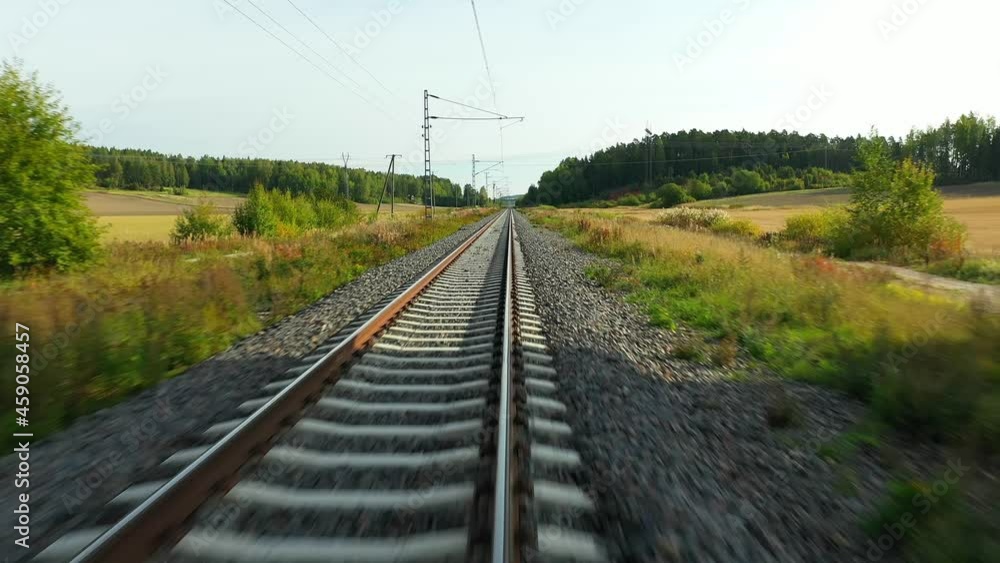 Poster High speed aerial drone view at low altitude moving forward following straight railroad tracks passing under bridge with agricultural fields on both sides, simulating train ride in summer time.