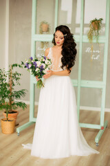 beautiful young girl in a white wedding dress holds a bunch of flowers in her hands. Gorgeous hair