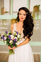 beautiful young girl in a white wedding dress holds a bunch of flowers in her hands. Gorgeous hair