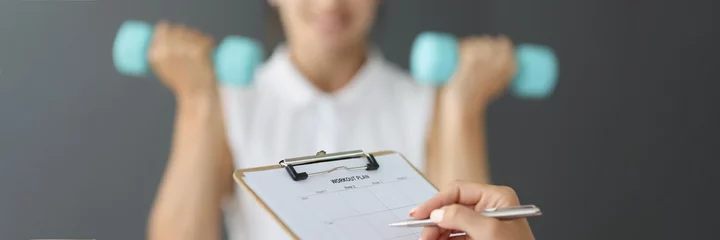 Fotobehang Persoonlijk Trainer filling out sports workout plan on background of woman with dumbbells closeup  © H_Ko