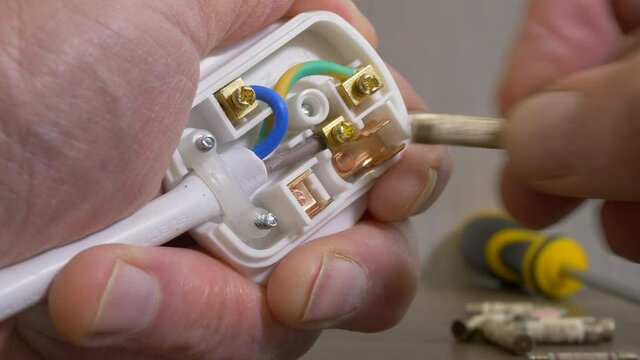 Closeup POV overhead shot of a man&rsquo;s left hand holding an open three pin British electrical plug, while the right hand pulls out a blown 13 amp fuse, then replaces it with a new one.