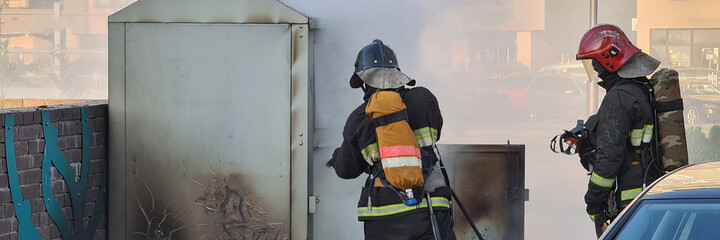 Fototapeta premium Firefighters extinguishing garbage can fire in car park