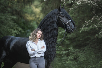 Beautiful young lady posing with a purebred friasian horse in the forest. - 459062627